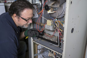 Techician looking over a gas furnace with a flashlight before cleaning it.